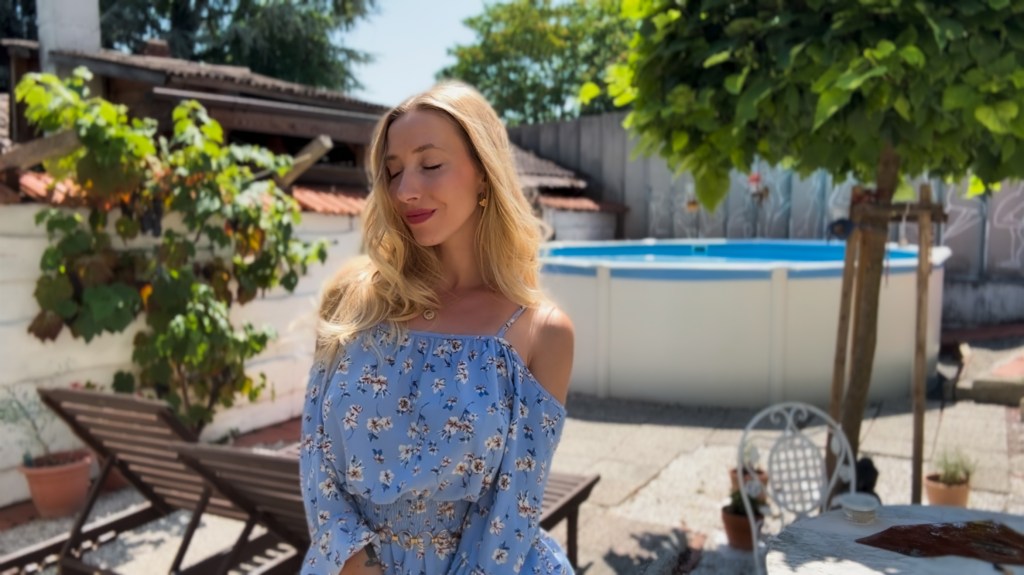 A blonde woman in a blue summer dress wearing an Atolea brand necklac and earrings